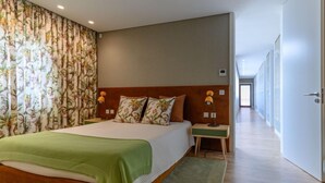 Una habitación de hotel moderna con una cama grande, cortinas estampadas con motivos florales, un plaid verde y un cabecero de madera.