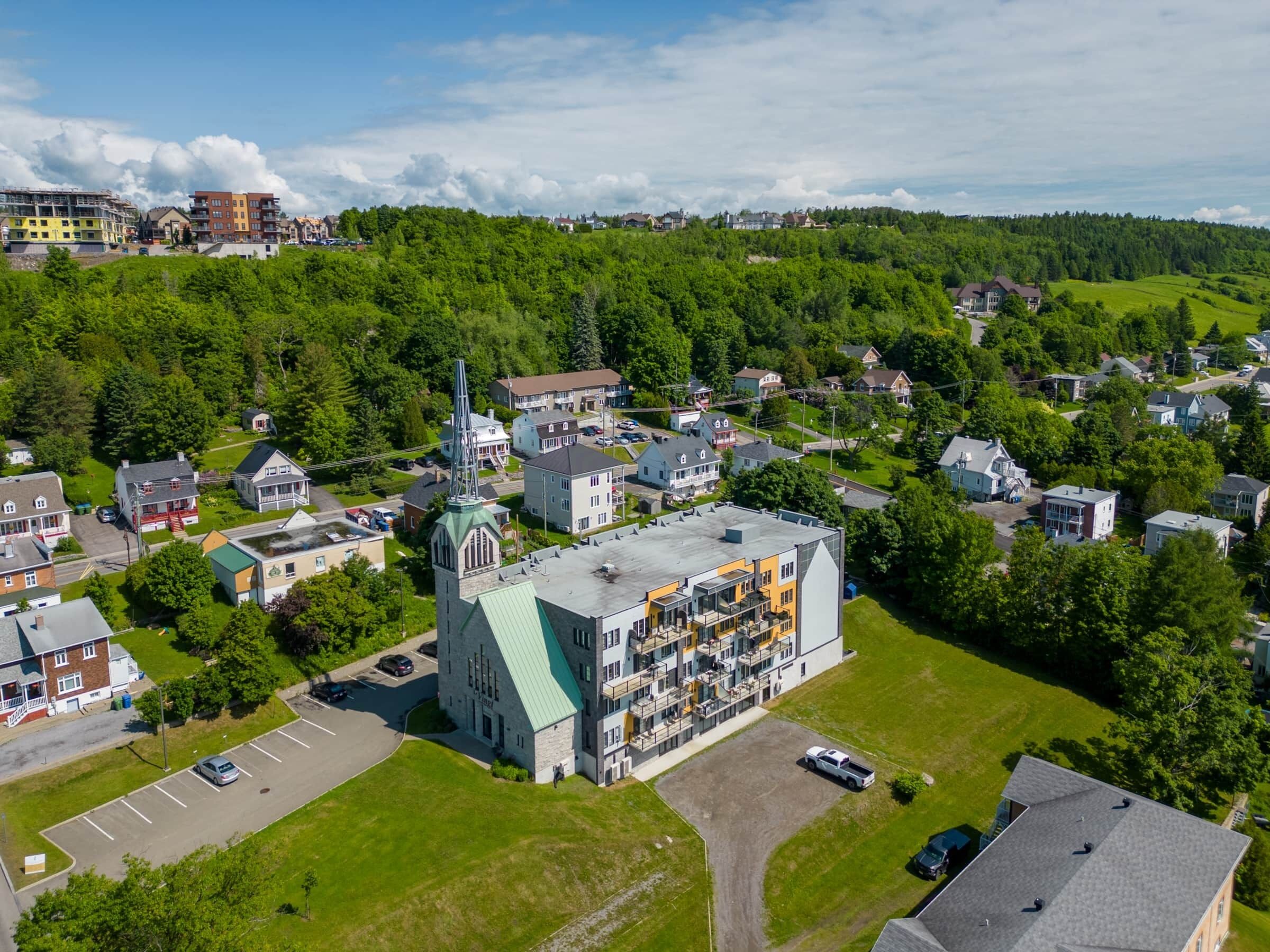 An aerial view of a residential area with a prominent church featuring a tall steeple, surrounded by houses and greenery.
