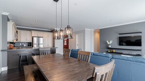 Una cocina moderna con armarios de madera, un refrigerador de acero inoxidable y un comedor con mesa y sillas de madera.