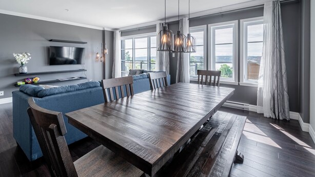 Un comedor moderno con una gran mesa de madera, sofá azul y televisor montado en la pared.