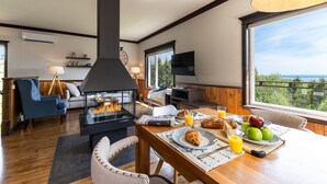 A cozy living room with a fireplace, a dining area with breakfast, and a large window offering a scenic view. - Hôtel à la maison - L'Escale, Spa et Fleuve (Les Éboulements)