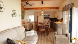 Een gezellige woonkamer met een bank, een eettafel met stoelen, een keuken met kasten en apparatuur, en een plafondventilator.