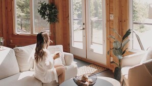 Une pièce spacieuse avec de hauts plafonds et de grandes fenêtres, un canapé blanc, une table basse ronde et une plante en pot.