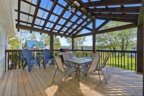 Eine überdachte Terrasse mit Tisch, Stühlen, einem Grill und Blick auf die Landschaft.
