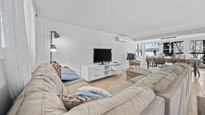 Een moderne woonkamer met een grote bank, een televisie en een eethoek met een tafel en stoelen.