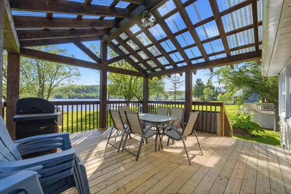 A covered patio with a table and chairs, a grill, and a view of a lake. - Hôtel à la maison - La Retraite du Lac Wallace (Saint-Herménégilde)