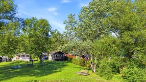 Een gelegenheid aan het meer met een gazon, een houten steiger en meerdere huizen met zichtbare terrassen en buitenmeubels.