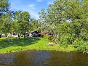 Une propriété au bord du lac, dotée d’une pelouse verdoyante, d’un quai en bois et de plusieurs maisons avec des terrasses apparentes et des espaces de détente en plein air.