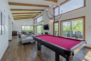 A spacious room with a pool table, a fireplace, and large windows offering a view of the outdoors.