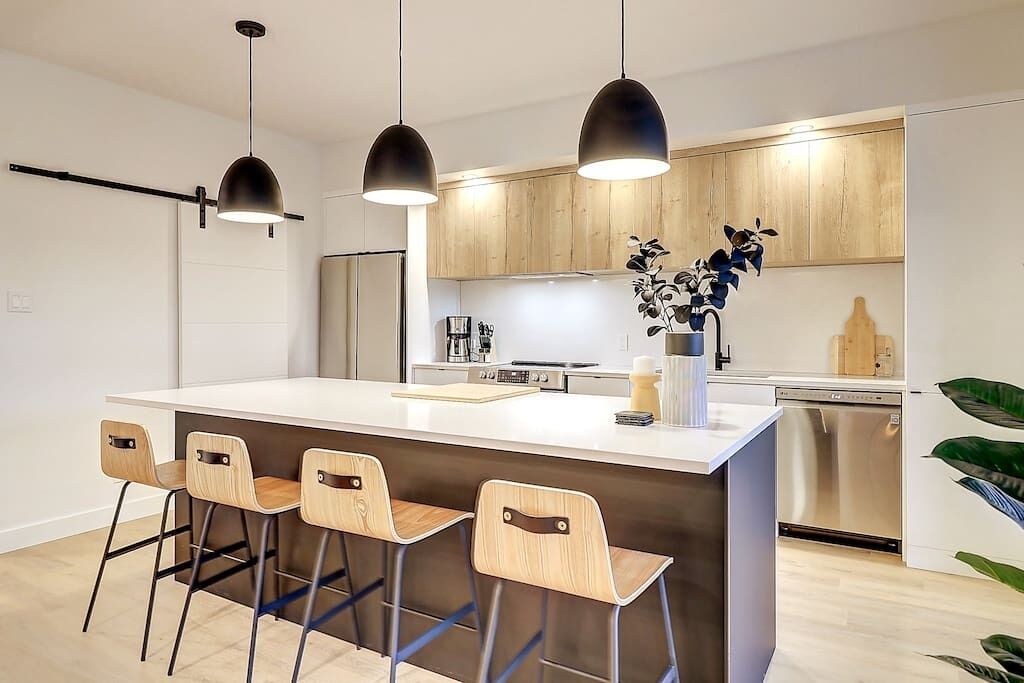 A modern kitchen with a central island, bar stools, pendant lights, and built-in appliances.