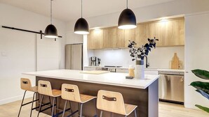 A modern kitchen with a central island, bar stools, pendant lights, and built-in appliances.