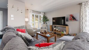 A modern living room with a sofa, armchairs, a coffee table, a TV, and a bookshelf. - Hôtel à la maison - Colombe du Cap, foyer et spa (Baie-Saint-Paul)