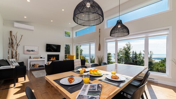 Un comedor moderno con una mesa de madera, sillas negras y vistas al mar a través de amplios ventanales.
