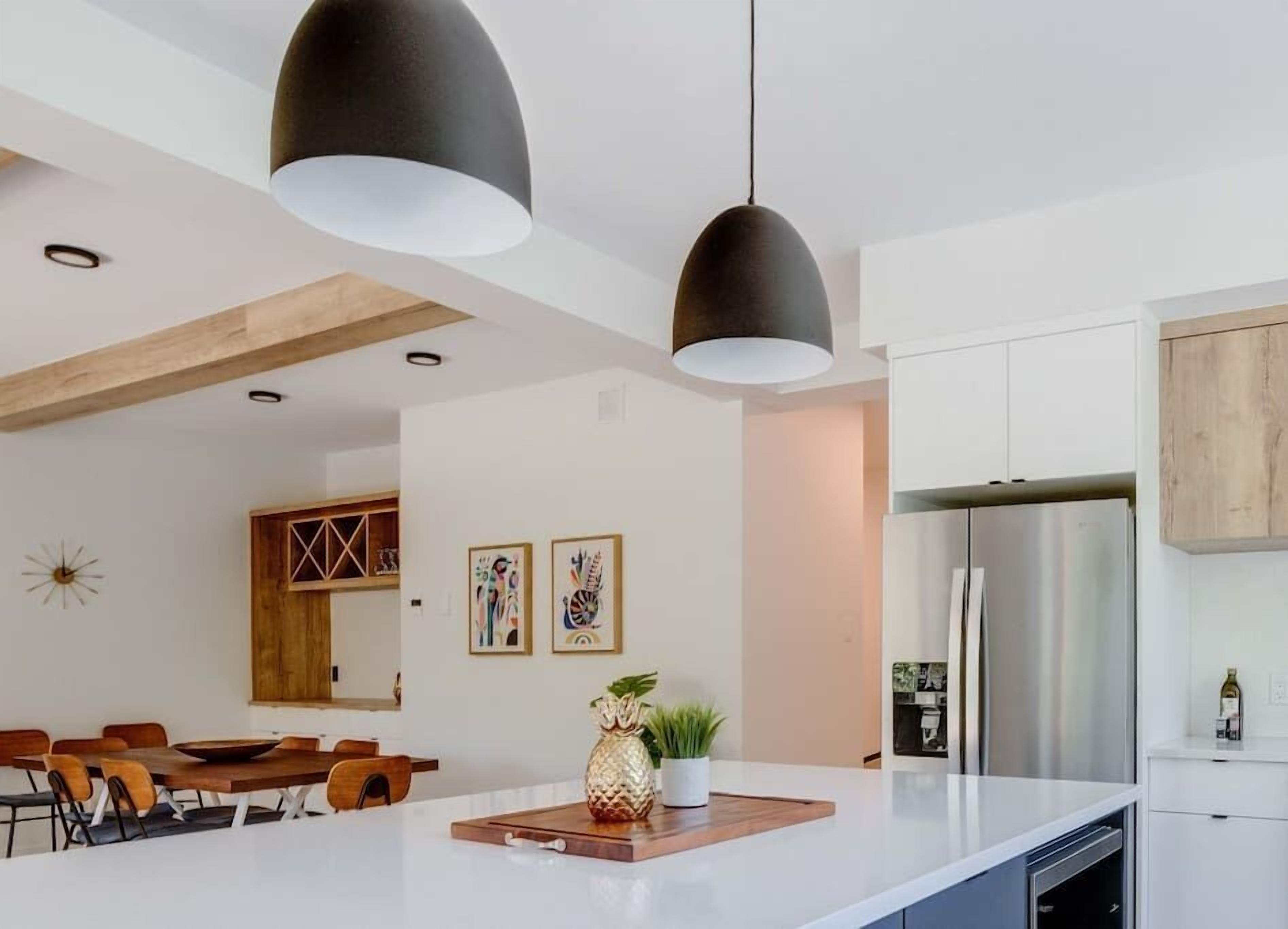 Une cuisine moderne avec des meubles blancs, un réfrigérateur en acier inoxydable et un coin repas comprenant des chaises en bois et une table blanche.