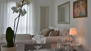 A hotel room with a bed, a table with glasses, a potted orchid, a radiator, and a painting on the wall.
