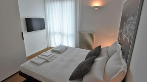 A modern bedroom with a bed, white linens, a mounted TV, and a radiator.