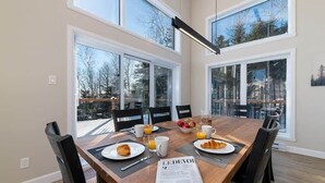 A dining area with a wooden table, chairs, breakfast items, and a newspaper. - Hôtel à la maison - Chez Fugère, spa et billard (Les Éboulements)