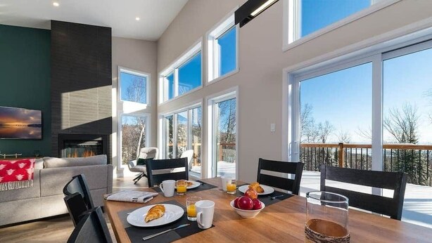 A dining area with a table set for breakfast, large windows, and a view of the outdoors. - Hôtel à la maison - Chez Fugère, spa et billard (Les Éboulements)