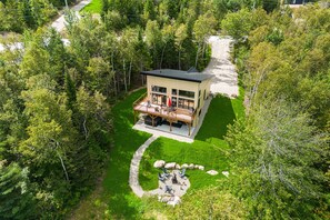 A modern house with a deck, surrounded by lush greenery and a gravel path.