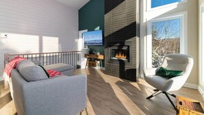 A modern living room with a fireplace, a sofa, a chair, and a television. - Hôtel à la maison - Chez Fugère, spa et billard (Les Éboulements)