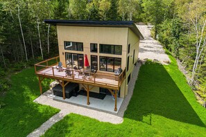 Un bâtiment moderne à deux étages, doté d’une terrasse, de grandes fenêtres et offrant une vue sur une zone boisée.
