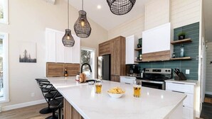 A modern kitchen with a large island, wooden cabinets, and pendant lighting. - Hôtel à la maison - Chez Fugère, spa et billard (Les Éboulements)