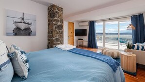 Ein Schlafzimmer mit einem großen Bett, einer Steinsäule, einem Fernseher, Meerblick und einem Balkon mit einem Stuhl.