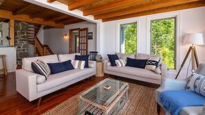 Ein geräumiges Wohnzimmer mit zwei Sofas, einem Couchtisch und einer Lampe. Im Hintergrund sind eine Holztreppe und eine Steinwand zu sehen.