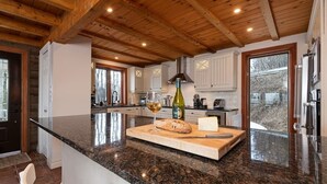 Eine Küche mit Granit Arbeitsplatten, Holzbalken und einer großen Kochinsel mit Schneidebrett, Weinglas und Brot.