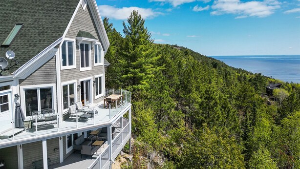 A two-story house with a balcony overlooking a forested hillside and a body of water. - Hôtel à la maison - Villa du Cap Blanc, spa et Vue (Saint-Irénée)