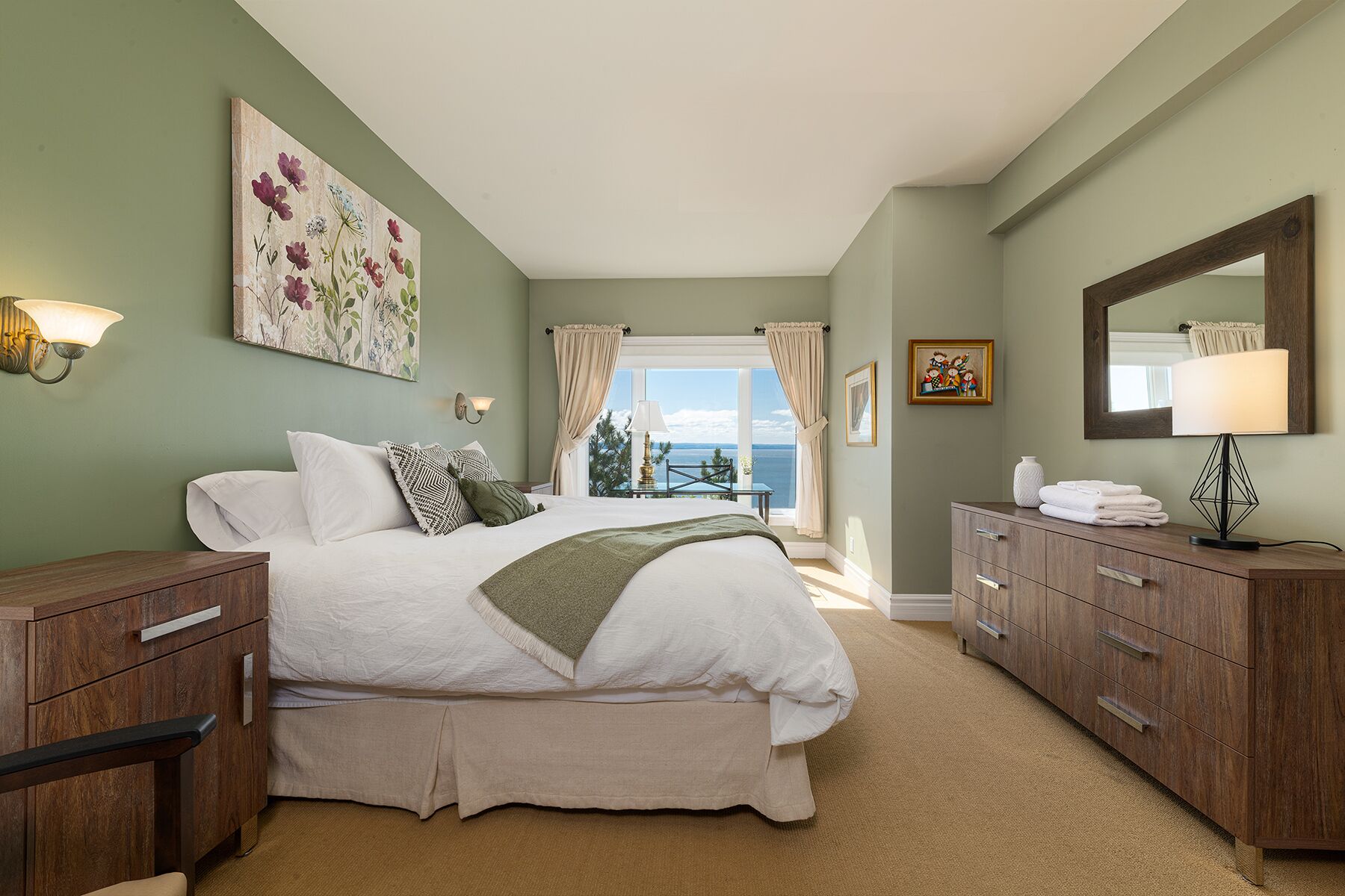 Ein Schlafzimmer mit einem großen Bett, einem Schminktisch, einem Spiegel und Blick aufs Meer.