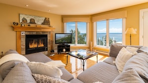 A living room with a fireplace, a television, and a sofa. - Hôtel à la maison - Villa du Cap Blanc, spa et Vue (Saint-Irénée)