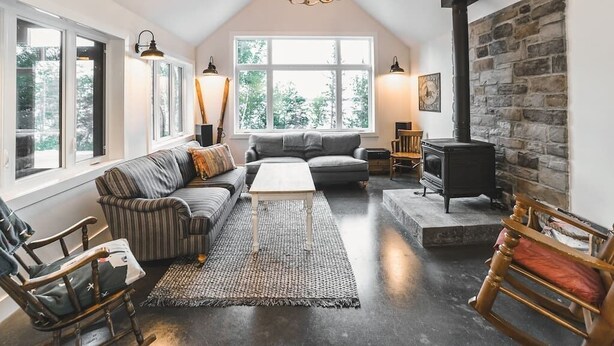 Una sala de estar estilo loft acogedora con pared de piedra, chimenea y un ventanal con vistas a la vegetación.