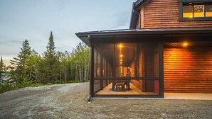Una cabaña de troncos moderna con un porche cubierto y un área de comedor visible en el interior.