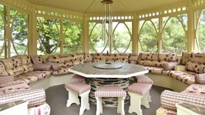 Un espacio al aire libre techado con una mesa redonda y bancos, rodeado de sofás y sillones acolchados.