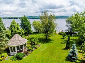 Un belvédère doté d’un toit en tuiles, entouré d’une végétation luxuriante et offrant une vue sur un lac.