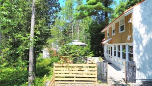 Puinen talo, jossa on kuisti, ja jonka ympärillä on tiheää kasvillisuutta ja puita.