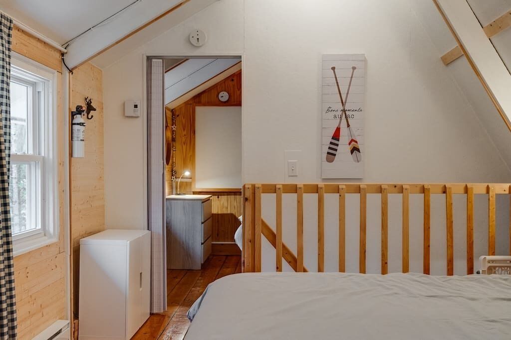 A cozy bedroom with a wooden headboard, a bed, a small white cabinet, and a wooden door leading to a bathroom.