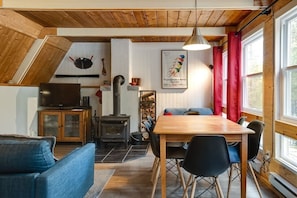 En hyggelig stue med træloft, pejs, fjernsyn og et spiseområde med bord og stole.