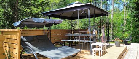 Un espacio de estar al aire libre cubierto, con una mesa, sillas, una butaca y una estructura de pérgola.
