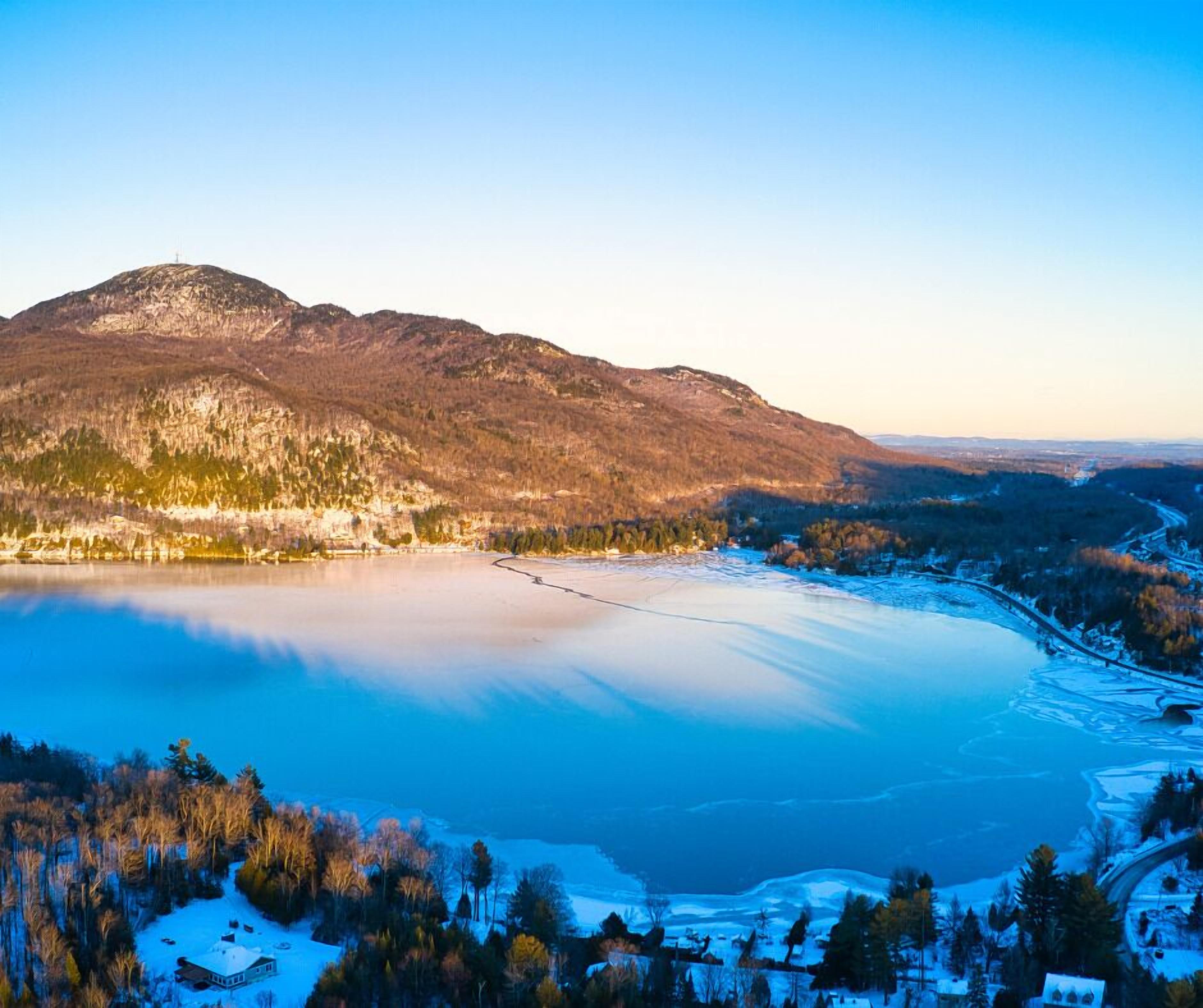 A panoramic view of a lake surrounded by mountains and a small settlement with snow-covered ground.