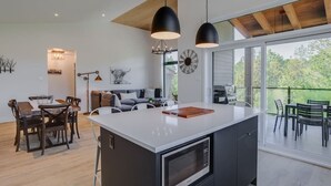 A modern kitchen with a large island, pendant lighting, and a dining area with wooden furniture. - Hôtel à la maison - La Cima (Orford)