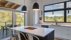 A modern kitchen with a large island, bar stools, pendant lighting, and a view of the outdoors. - Hôtel à la maison - La Cima (Orford)
