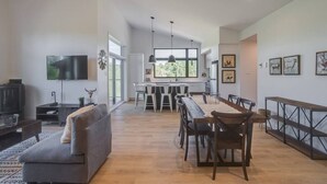 A spacious living area with a sofa, dining table, and chairs, a kitchen in the background, and artwork on the walls. - Hôtel à la maison - La Cima (Orford)