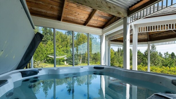 Un bain à remous doté d’un plafond en bois et de grandes fenêtres donnant sur un jardin.