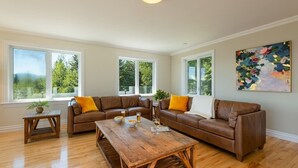 Un salon spacieux avec une table basse en bois, deux canapés en cuir marron ornés de coussins jaunes et une grande fenêtre offrant une vue sur la verdure.