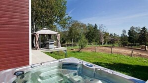 Ein Whirlpool mit mehreren Düsen, eine Terrasse mit Tisch und Stühlen sowie ein umzäunter Garten mit Bäumen und einem Pferd im Hintergrund.