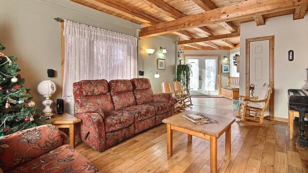 Ein gemütliches Wohnzimmer mit Holzbalkendecke, einem roten Sofa mit Muster, einem Couchtisch und einem Weihnachtsbaum.