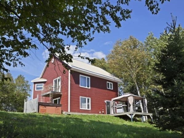Una casa rossa con un balcone, immersa tra alberi e un cielo sereno.