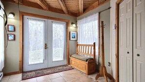 Ein Zimmer mit Holzbalken, einer Bank, einer an der Wand lehnenden Gitarre und einer Tür mit Fenster.